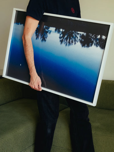 Fotografie bellezza quotidiana: un uomo tiene una stampa incorniciata mentre si trova su un divano.